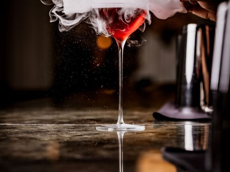 Hand popping the bubble to create a smoke effect to the Turkey, Sphere cocktail in a martini glass at The May Fair Bar