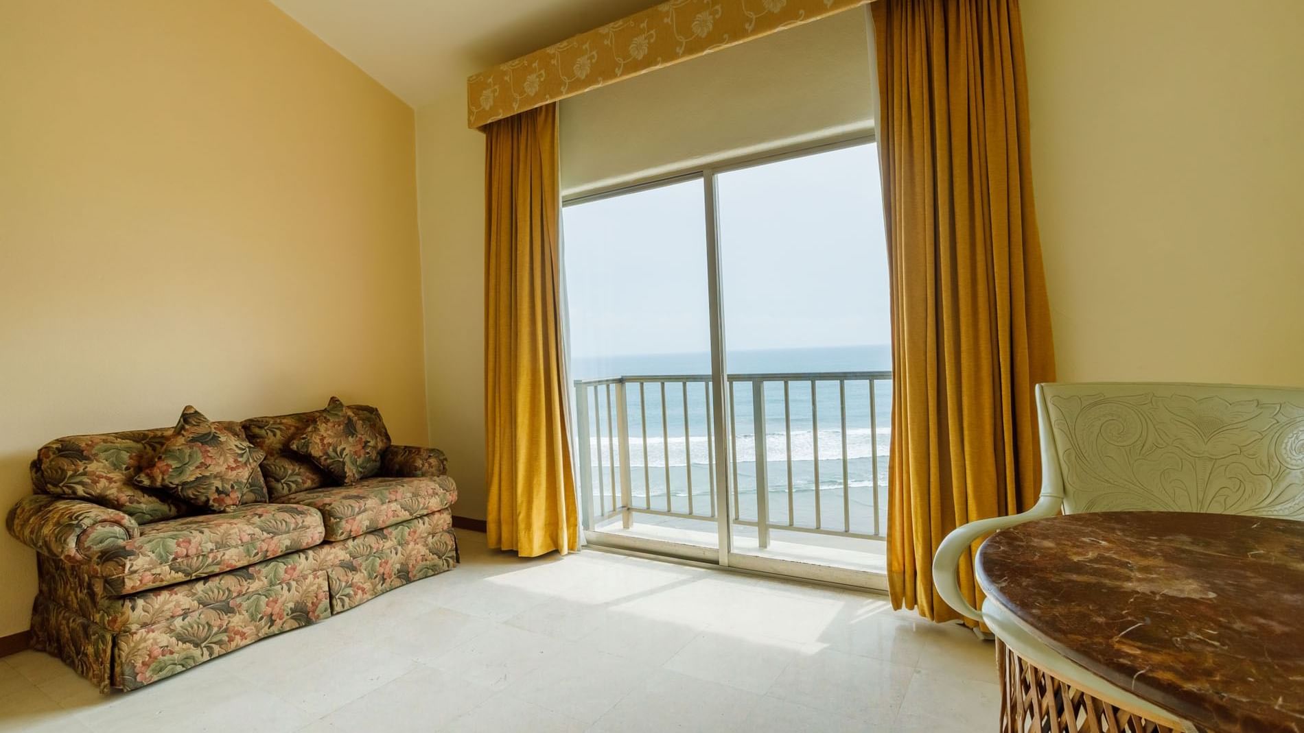 Sala de estar con sofá y mesa, y balcón con vista al mar.