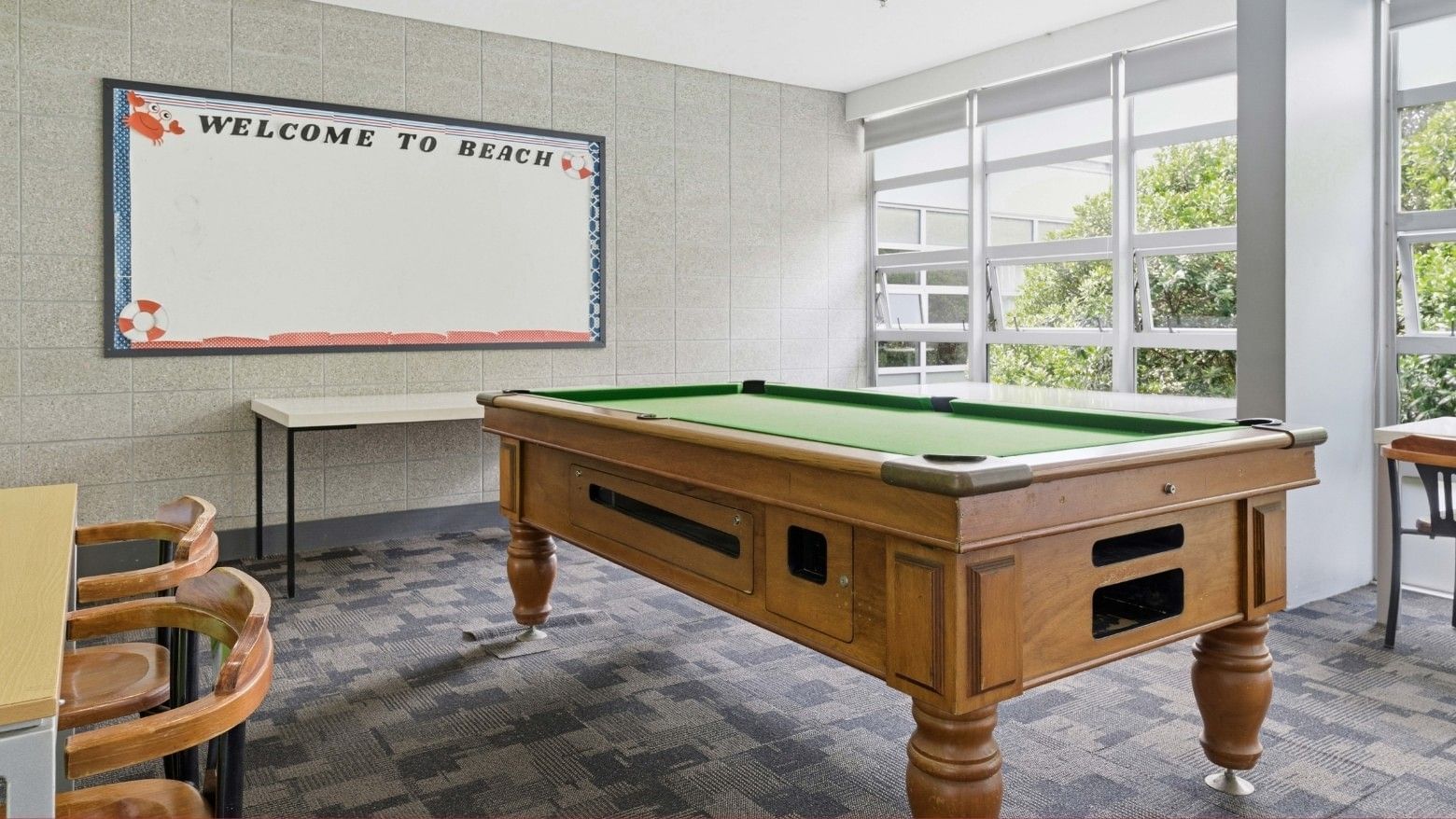 A pool table and chairs in a room with a whiteboard at Student Living Auckland – Anzac.