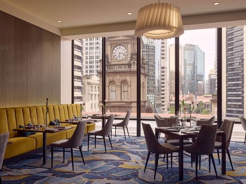 Restaurant Bistro Suzette with yellow banquette seating and cityscape view through large windows at Sofitel Brisbane Central