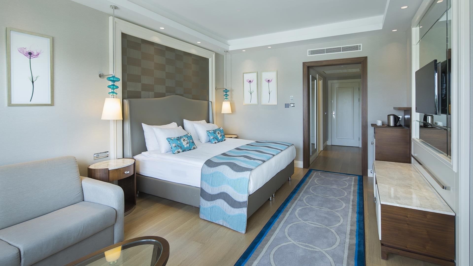 Titanic Deluxe Golf Belek’te ahşap zeminli Superior Oda’da yatağın yanında konumlandırılmış dinlenme koltuğu.