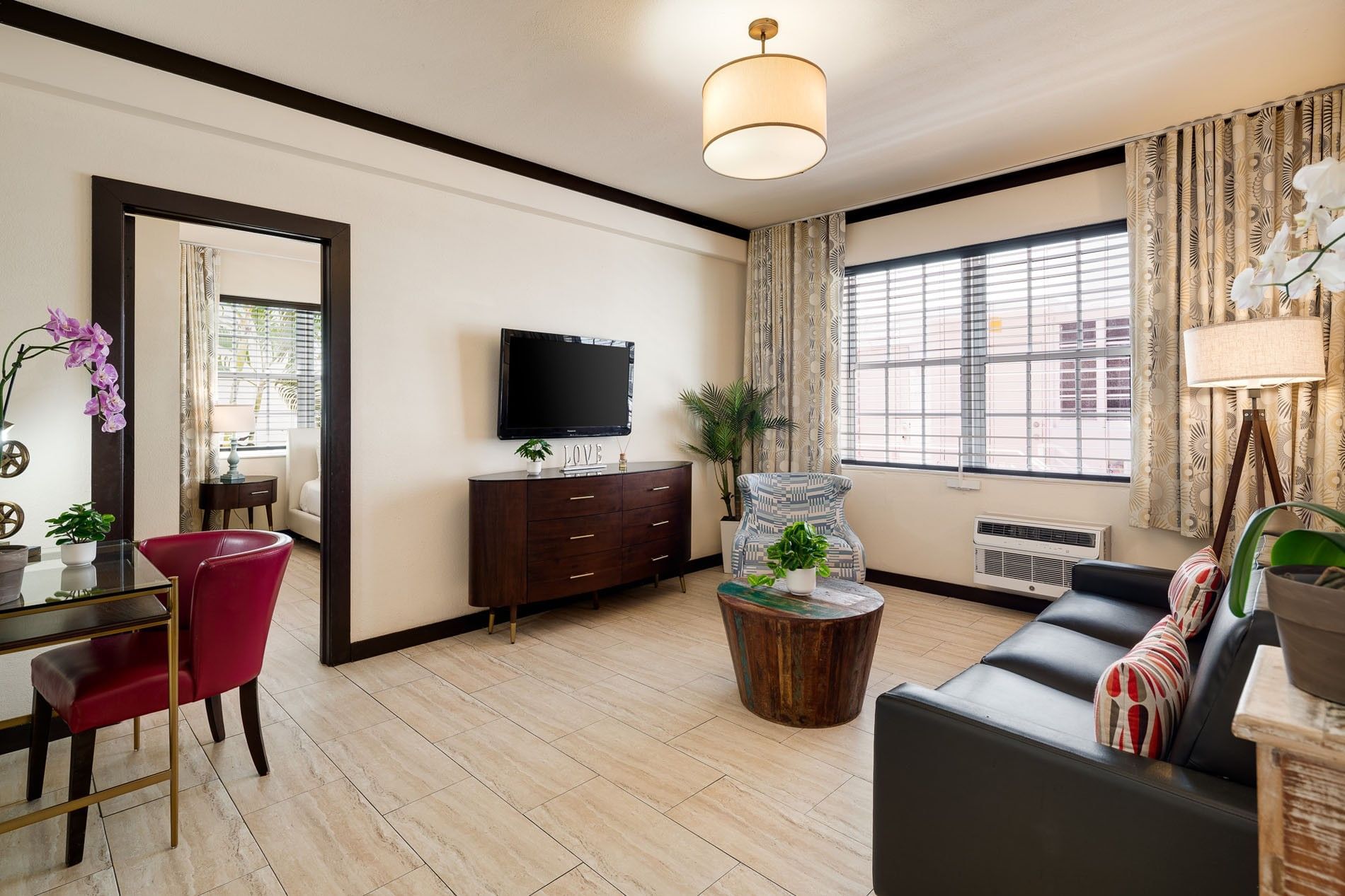 A hotel lobby with a black leather sofa, a wooden coffee table, a TV on a dresser, and a lamp.