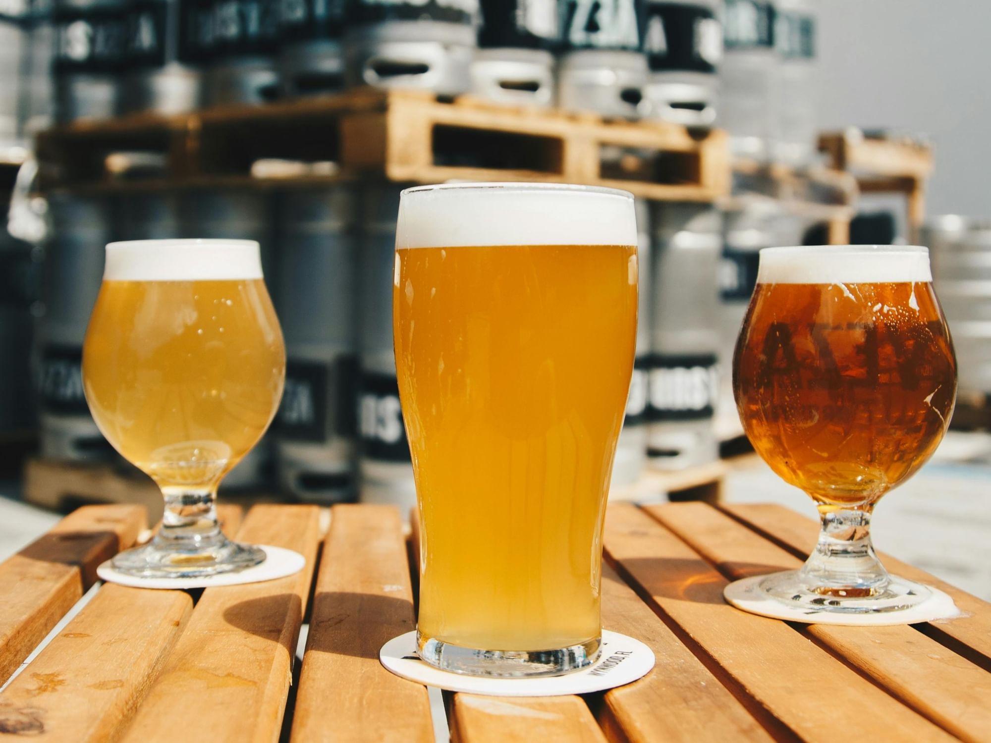 Three different glasses of beer sitting atop a wooden table in a bar.