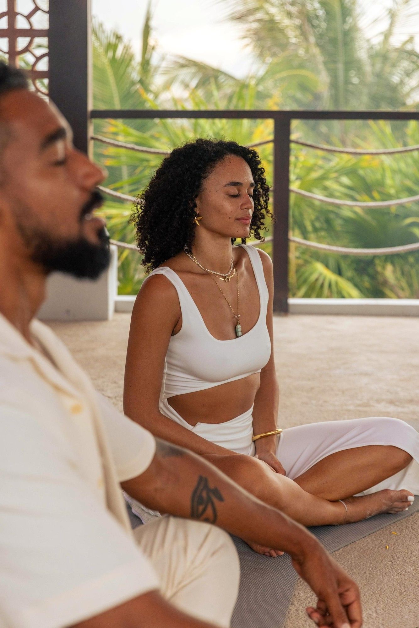 A man and woman meditate peacefully sitting cross-legged in a semi-outdoor yoga space at La Zebra Hotel