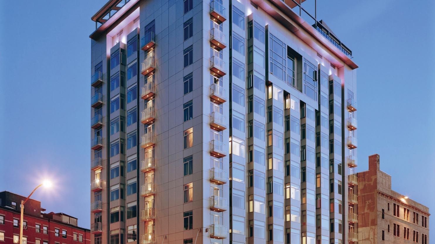 Gansevoort Meatpacking NYC's modern illuminated hotel building with glass facade and rooftop terrace at dusk.