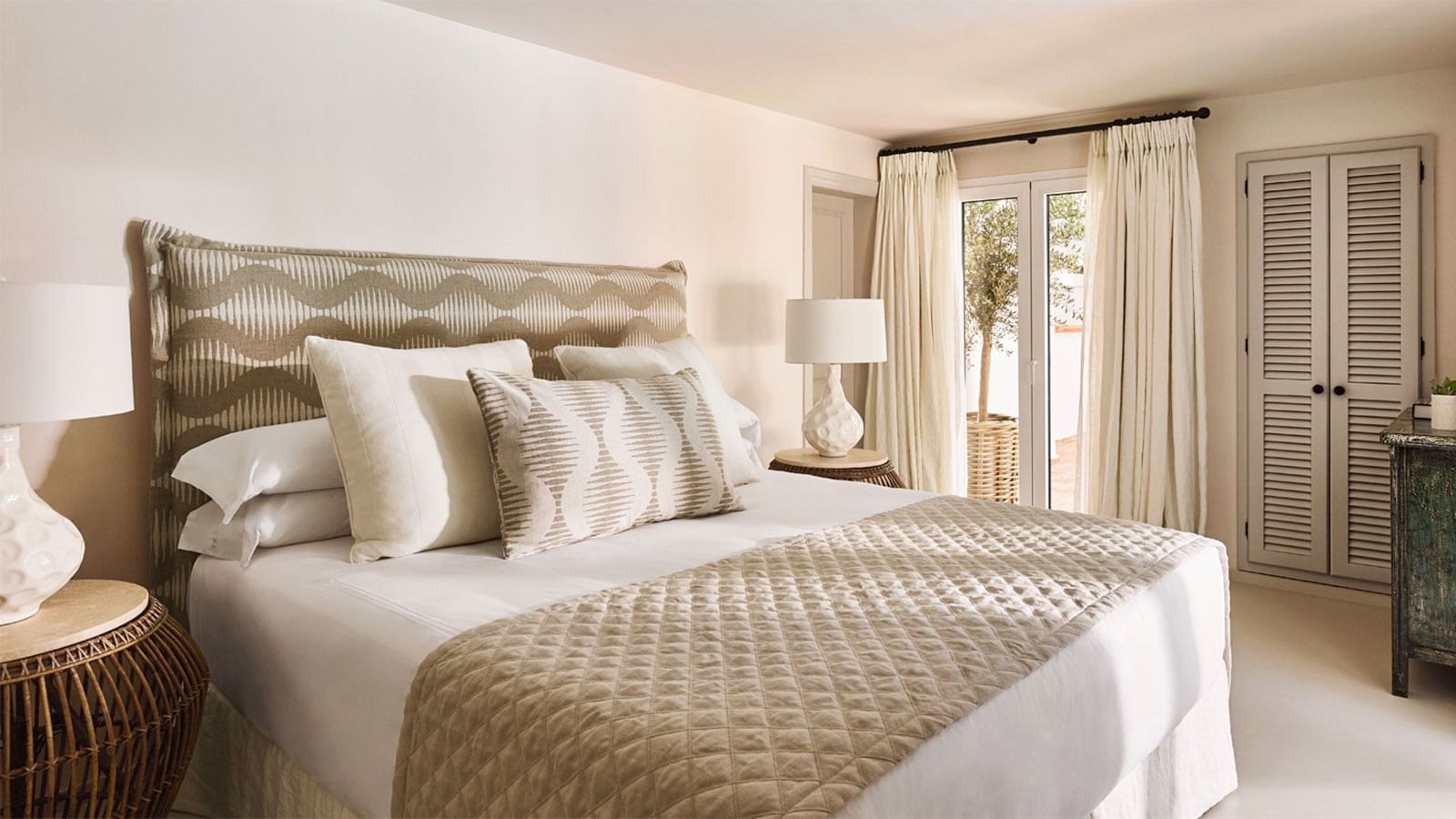 Bed in Casabel with a patterned headboard, neutral quilted coverlet, & doors opening to terrace at Marbella Club