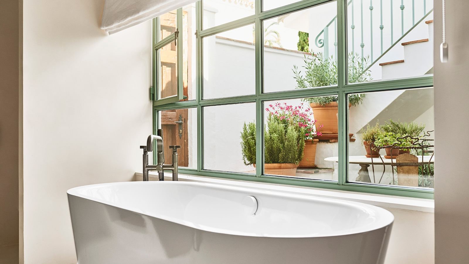 Bathroom featuring a soaking tub by a large green-paned window looking into a courtyard at the Marbella Club