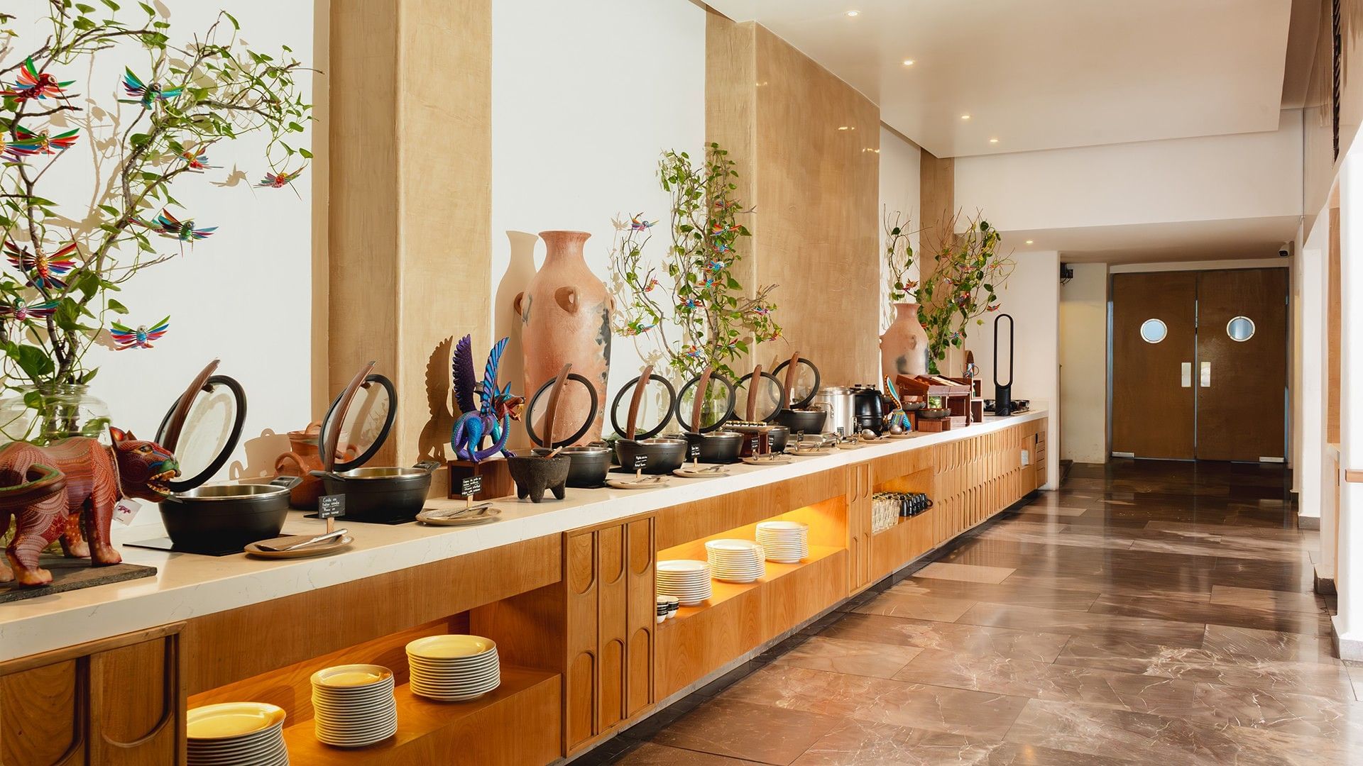Luxurious buffet setup with ceramic pots, vibrant decorations, & lush greenery in Chez Binni at Camino Real Zaashila Huatulco