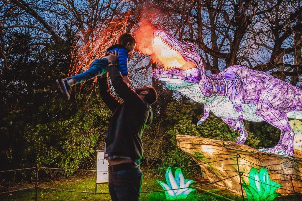 Father lifting son near illuminated dinosaur sculpture at Lake Buena Vista Resort Village & Spa