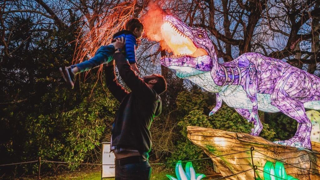 Father lifting son near illuminated dinosaur sculpture at Lake Buena Vista Resort Village & Spa