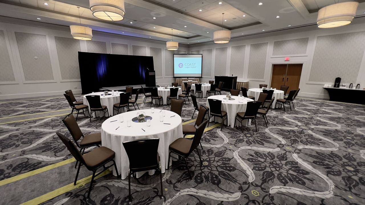 Ballroom with round tables, chairs, stage, podium and presentation screen