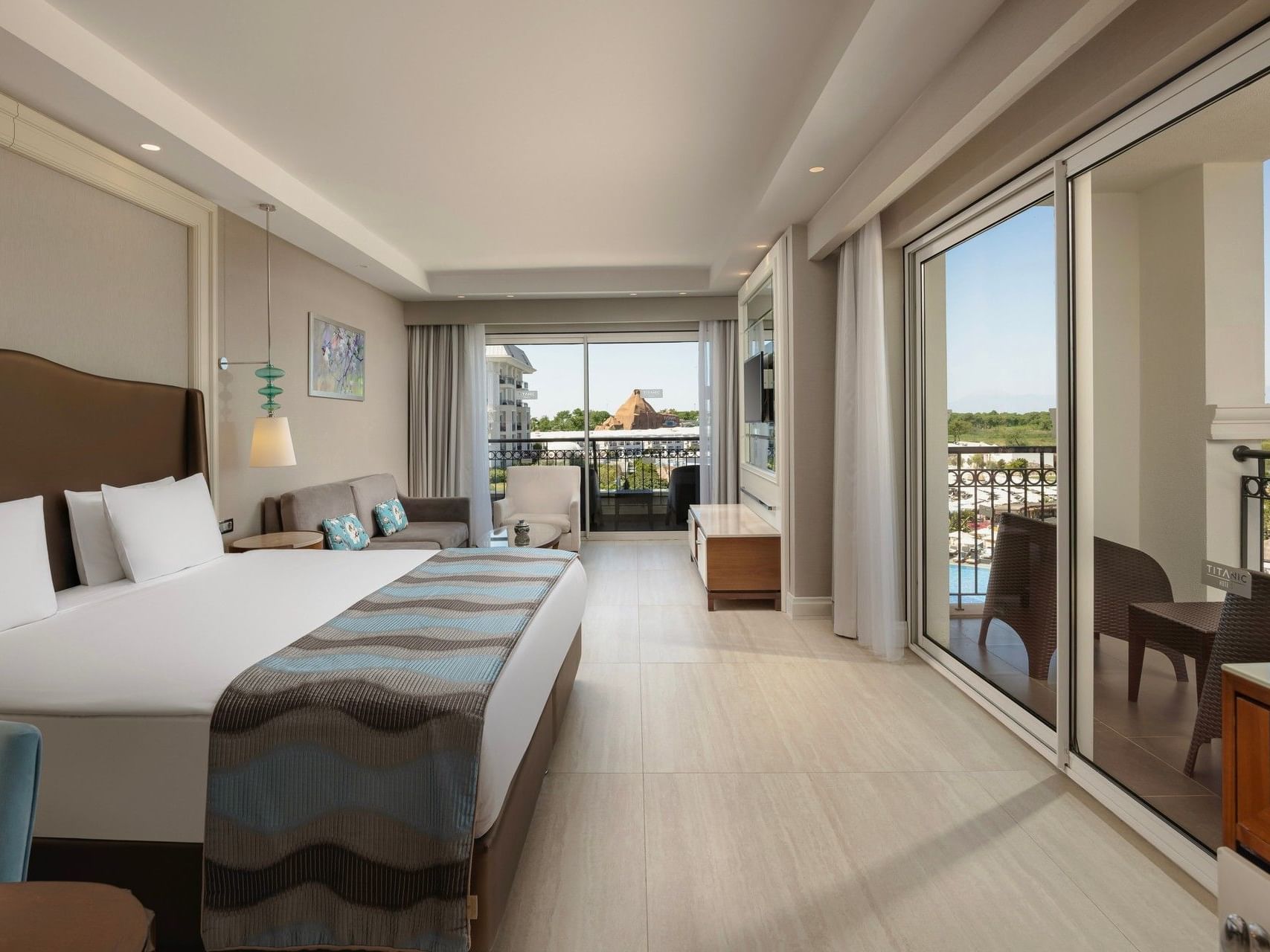 Spacious hotel room with king bed, seating area, and balcony overlooking golf course at Titanic Deluxe Golf Belek
