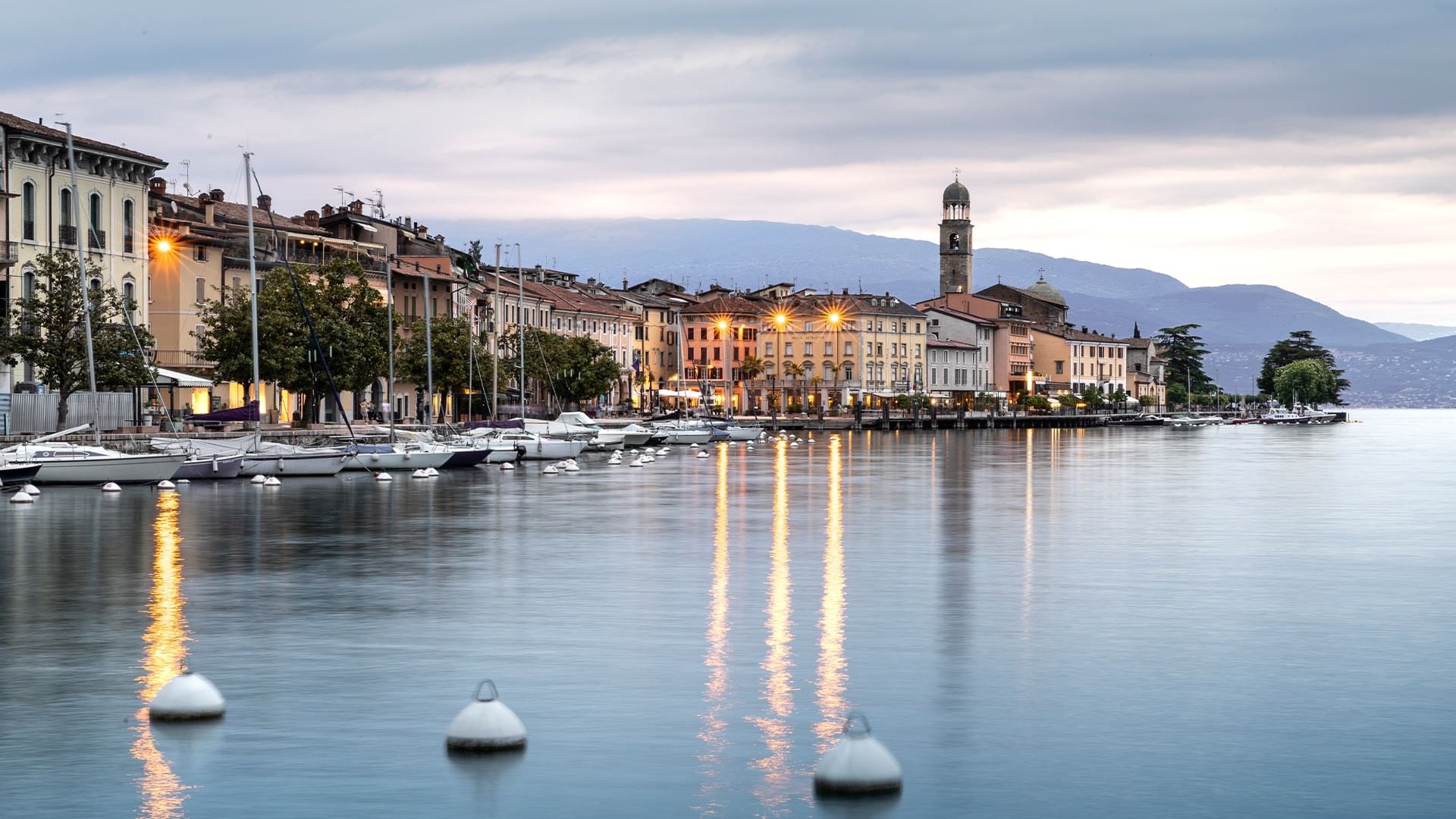 Molti yacht ormeggiati lungo un molo, con edifici e una torre sullo sfondo.