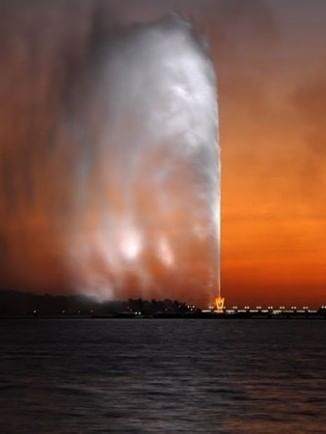 King Fahd's Fountain by the dark sea under a vibrant orange sunset near Warwick Jeddah Hotel & Spa