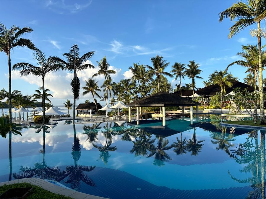 Tropical pool with palm trees and pavilions under a blue sky at Warwick Le Lagon Vanuatu.