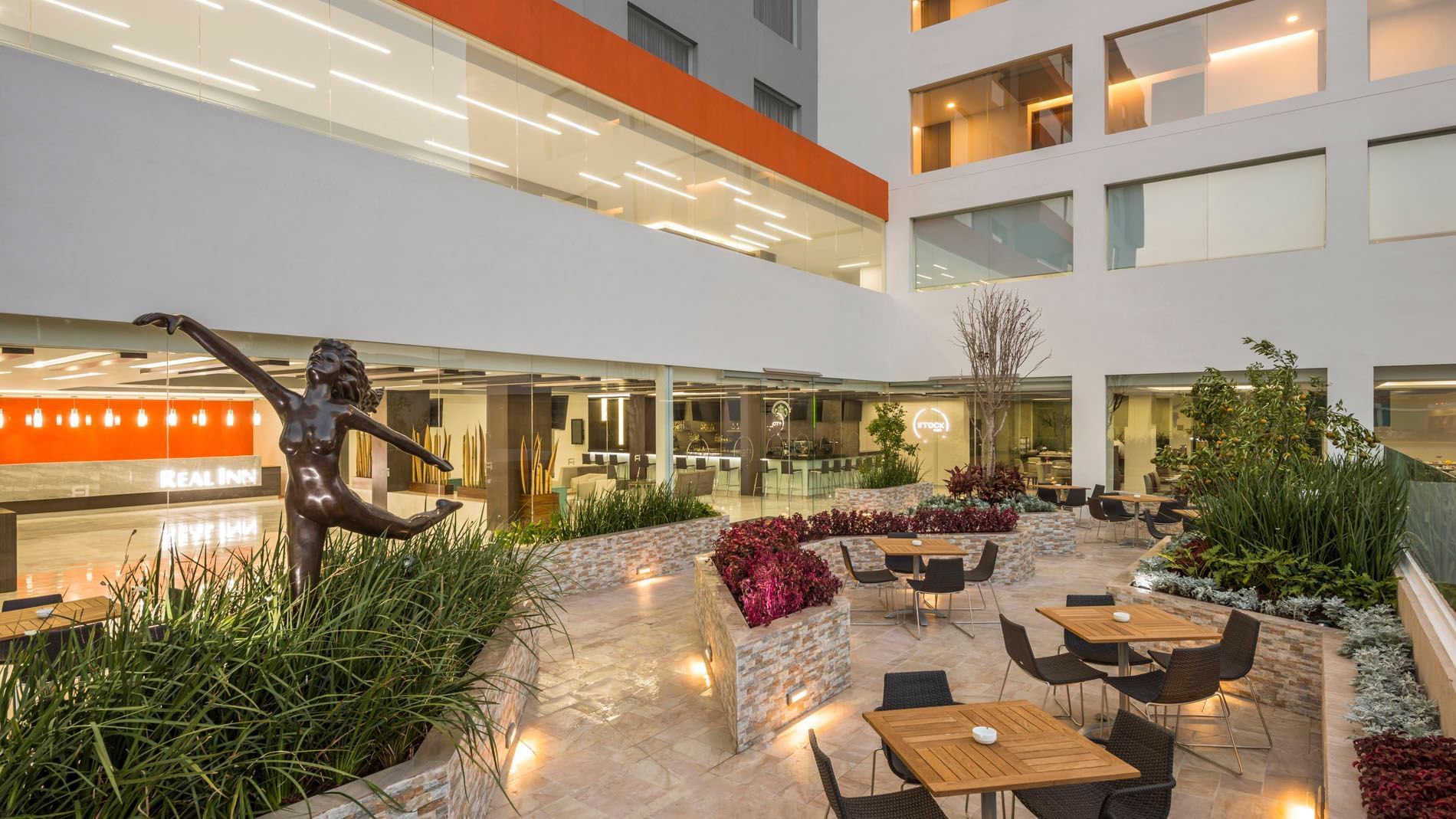 Scenic outdoor patio featuring a bronze dancer statue, lush plants, and café seating at Real Inn Celaya