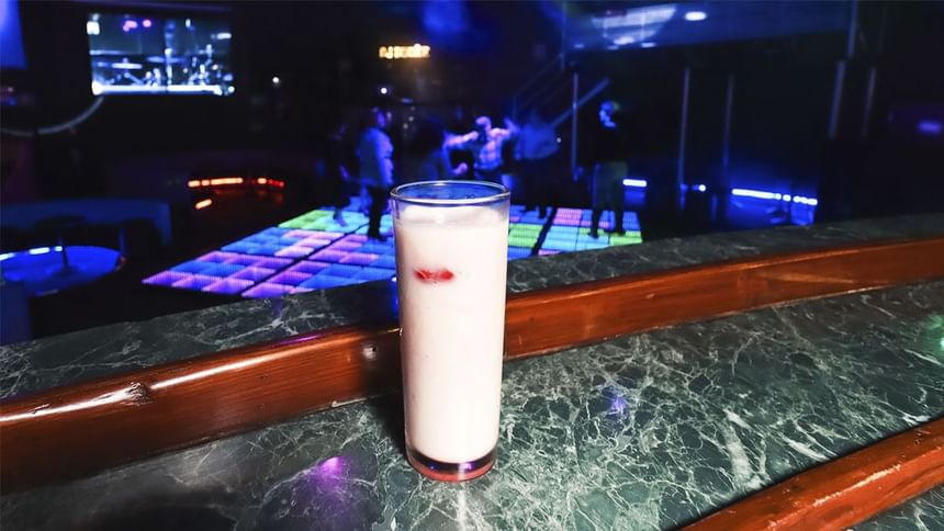 Cóctel rosa cremoso sobre barra de mármol oscuro con pista de baile iluminada al fondo en El Rollo de Araiza Palmira