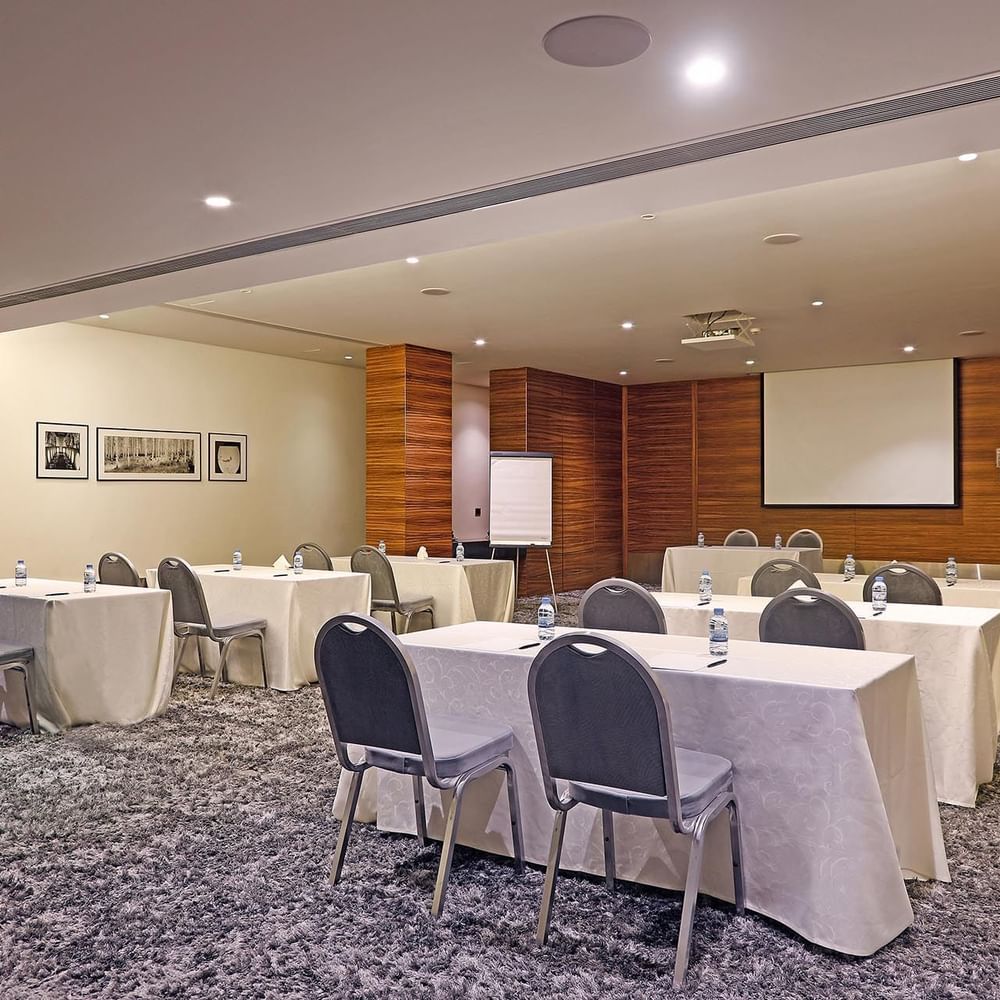 Grey chairs by tables under a projector screen near wood-paneled pillars in Emerald Room at Warwick Stone 55 - Beirut