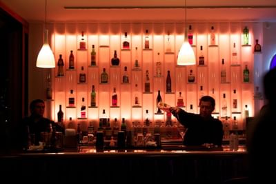 Barman sirviendo bebidas junto a muro de botellas iluminado bajo lámparas colgantes en Tramonto Bar & Terrace