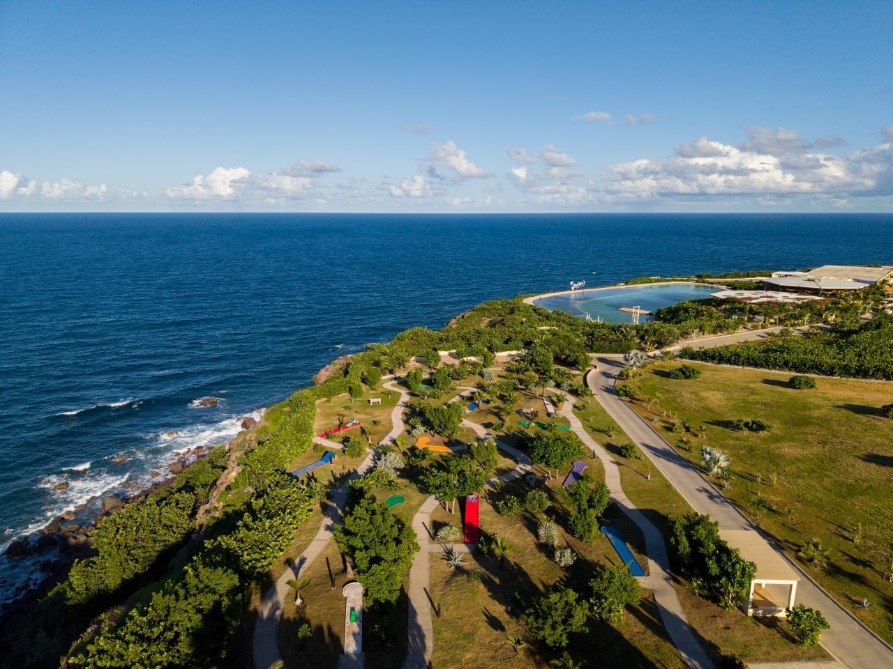 Aerial drone view of a colorful mini golf course along the rocky coastline near the blue ocean at Golden Rock Resort