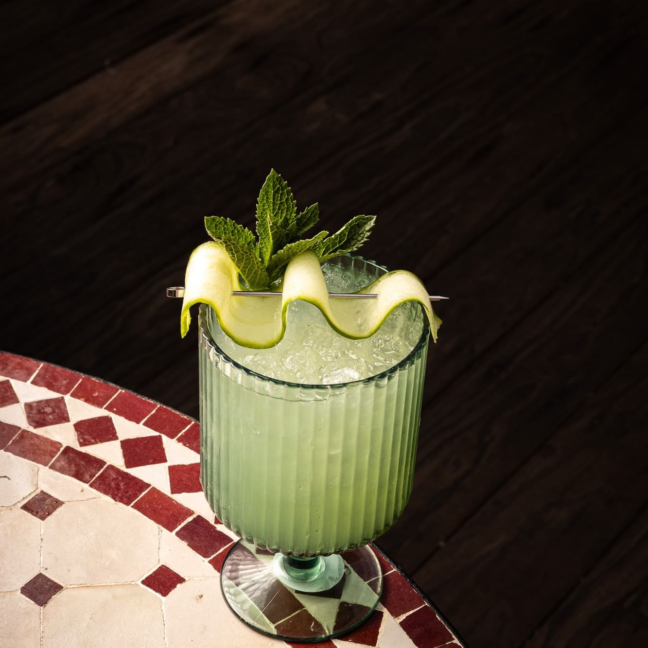 Green cocktail with cucumber ribbon and mint garnish on tiled table for Tequila Tuesdays at The Roof
