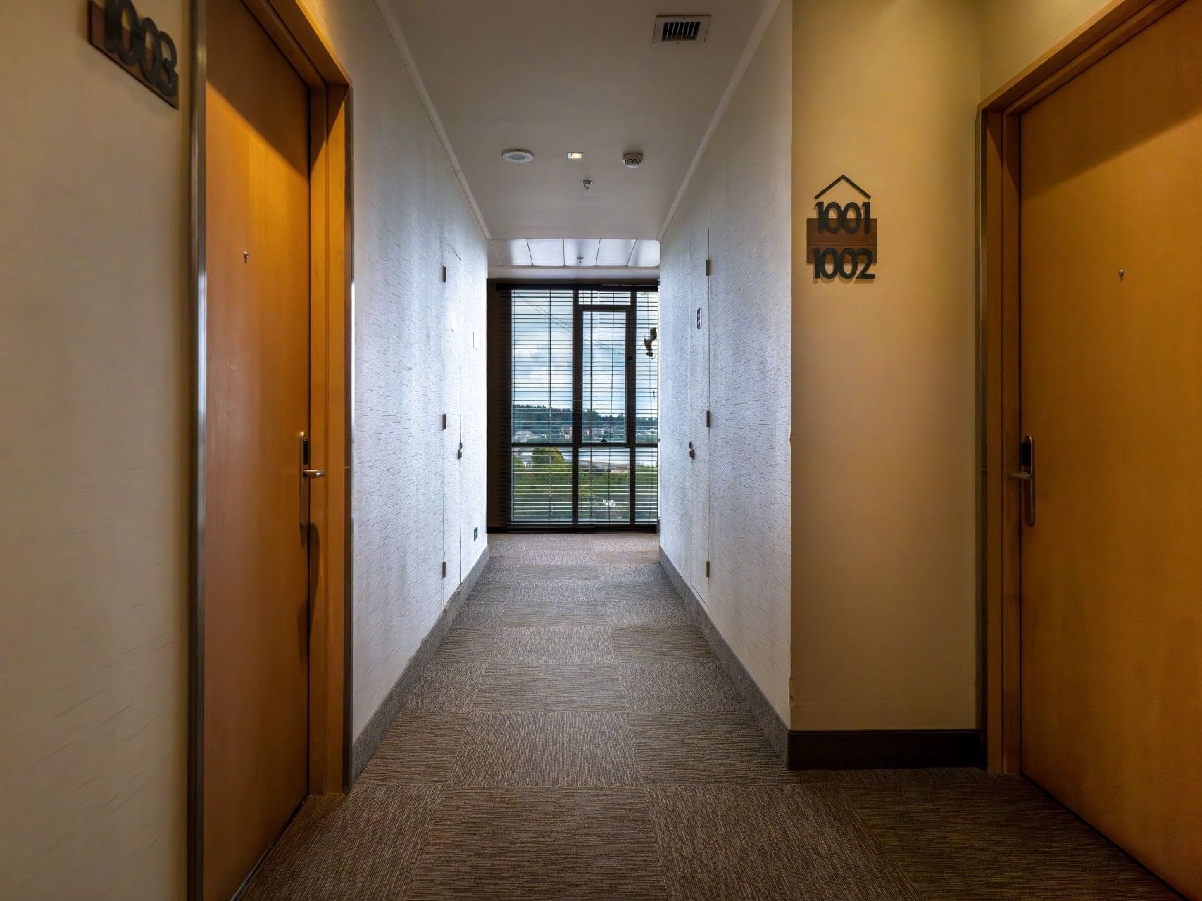 Largo pasillo con puertas de madera y suelo enmoquetado en el hotel HCC Costanera Concepción.