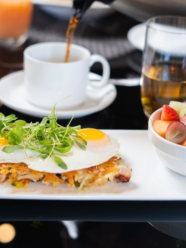 Sunny-side eggs by a fruit bowl under coffee being poured in The Landmark - Breakfast at Warwick Melrose Dallas