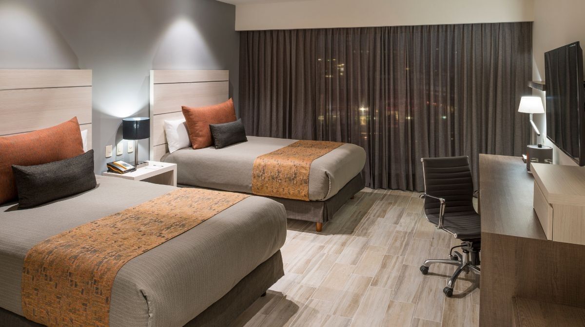 Modern double room at Camino Real Pedregal Mexico, featuring two beds, orange accents, and a sleek work desk area