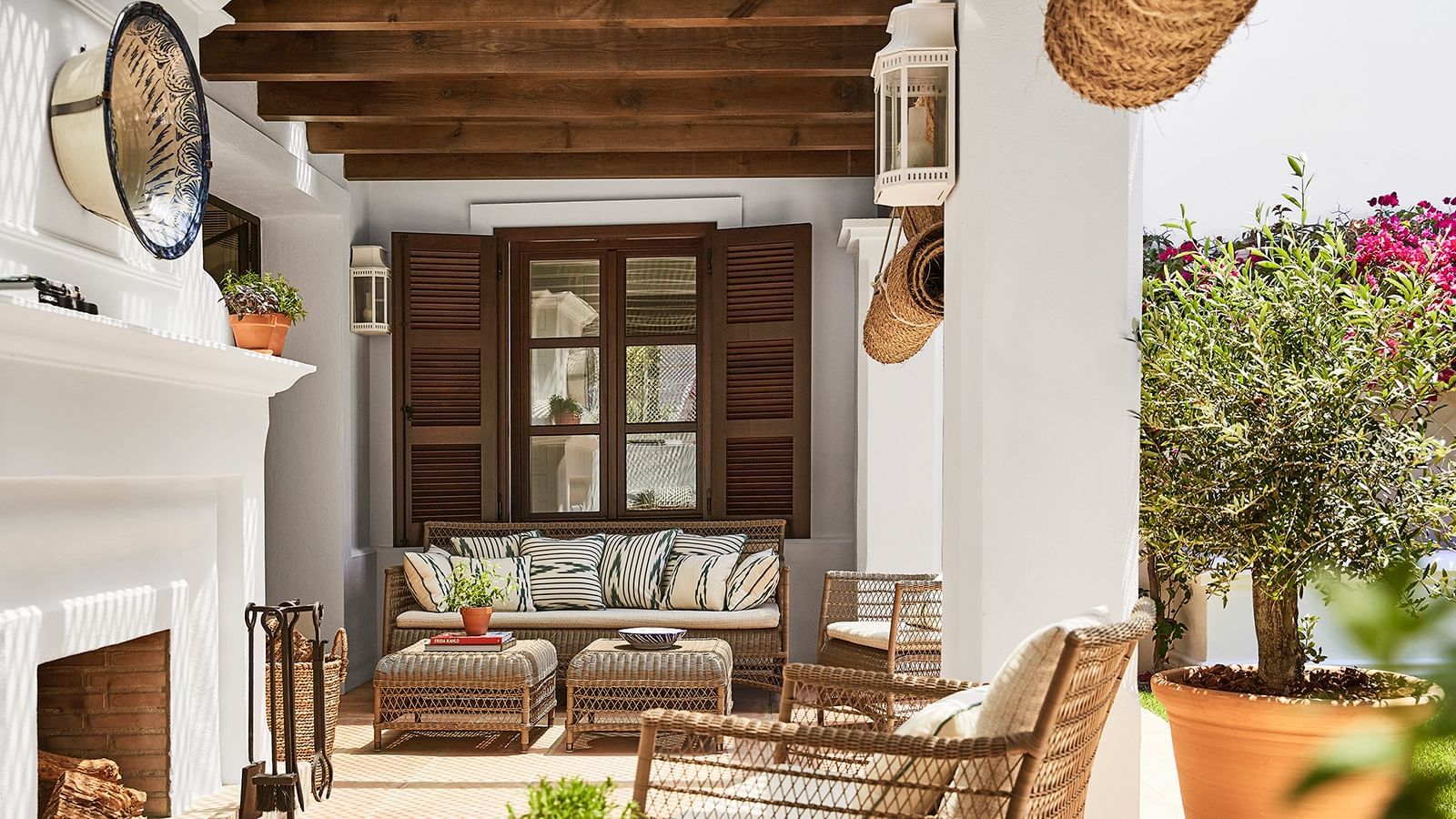Patio with a rattan sofa and chairs set under dark wood beams by a shuttered window at the Marbella Club