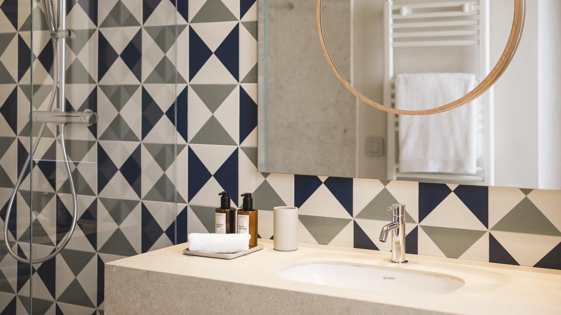 Bagno con doccia, lavabo, asciugamani, due bottiglie e uno specchio con asciugamani.