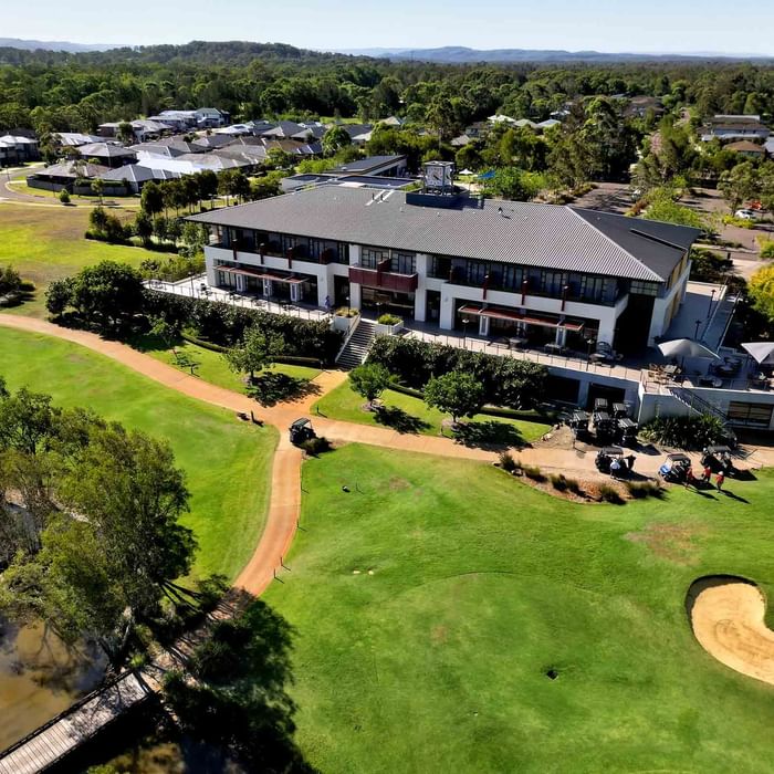 Aerial view of Mercure Kooindah Waters with a green course, sand bunkers, and a pond, under a clear sky