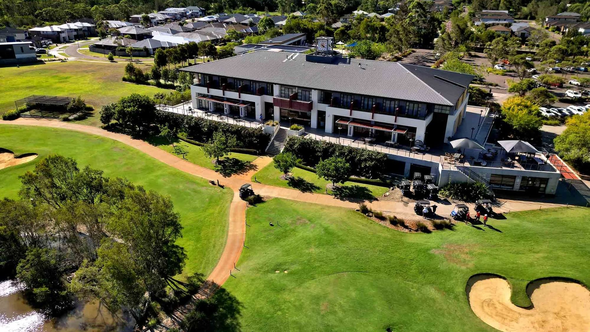Aerial view of Mercure Kooindah Waters with a green course, sand bunkers, and a pond, under a clear sky