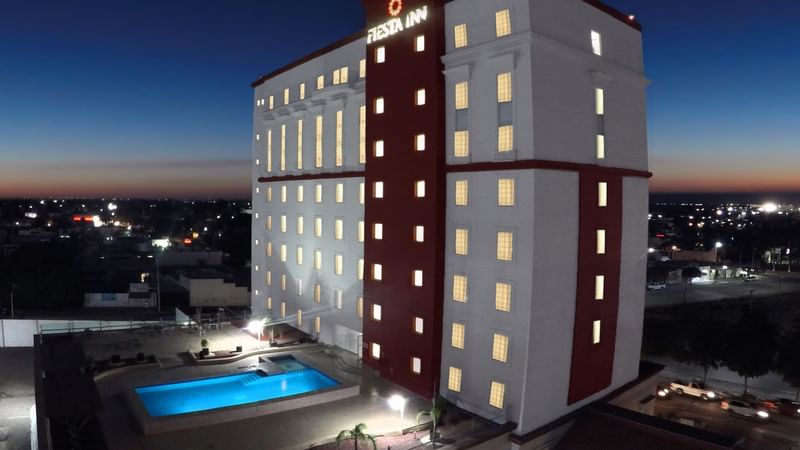 Brightly lit Fiesta Inn Ciudad Obregón at dusk, featuring a pool and surrounding city lights