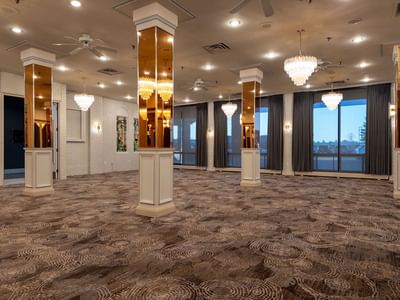 Large room at Carriage House Hotel with carpeted floor, ceiling fans, chandeliers, and glass windows with curtains.