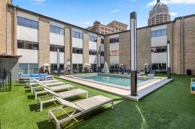 Modern courtyard at The Riverwalk Plaza Hotel with an outdoor pool, lounge chairs, and shaded cabanas under a blue sky