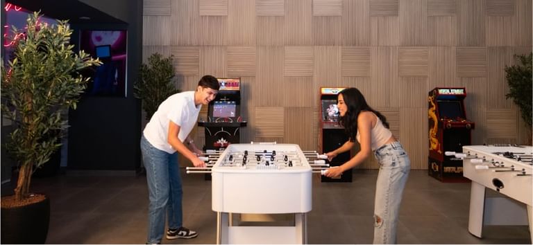 Friends smiling and competing the foosball game inside the Level Up - Indoor Gaming Hub at DAMAC Maison Aykon City