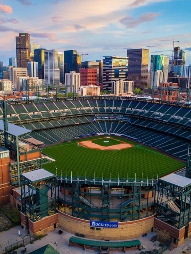 Aerial view of Coors Field Stadium by city buildings under a sunset sky near Warwick Denver