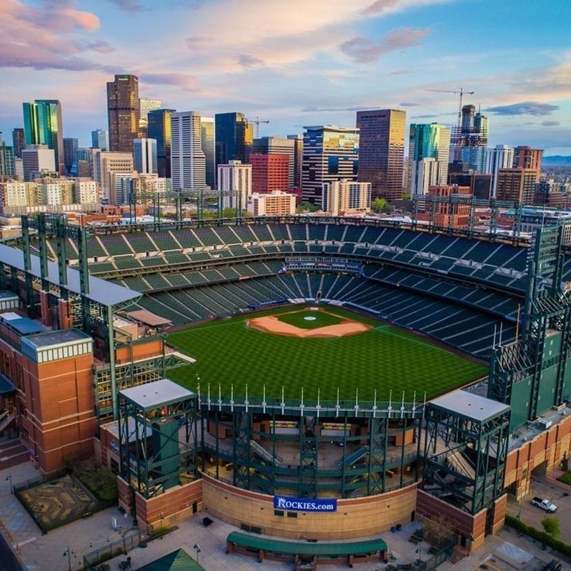 Aerial view of Coors Field Stadium by city buildings under a sunset sky near Warwick Denver