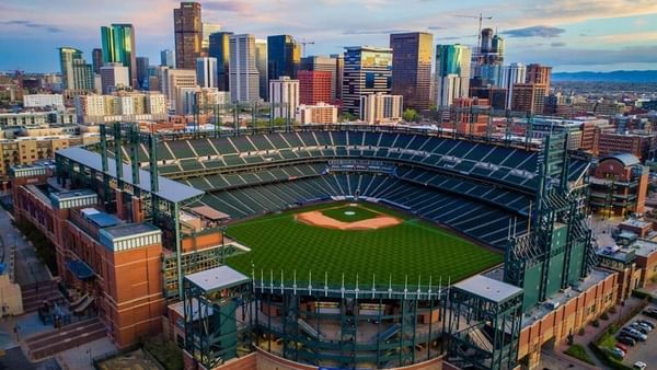 Aerial view of Coors Field Stadium by city buildings under a sunset sky near Warwick Denver
