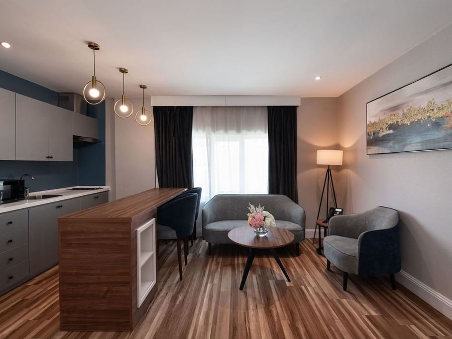 Grey sofa and armchair by a round coffee table near a wooden breakfast bar in Family Suite Sea View at Warwick Al Jubail