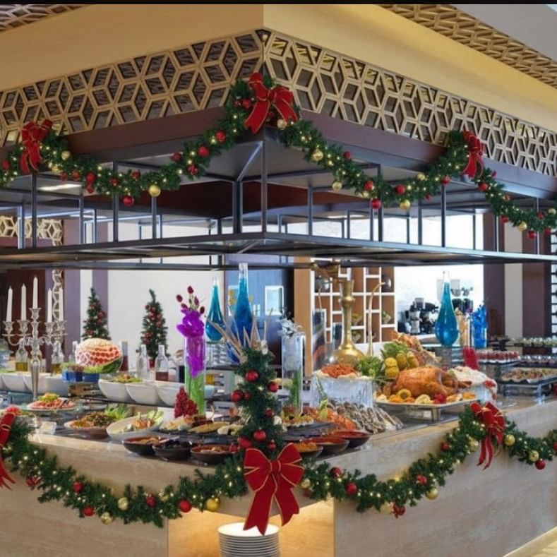 A festive buffet table decorated with Christmas garlands, bows, and ornaments, showcasing various dishes.