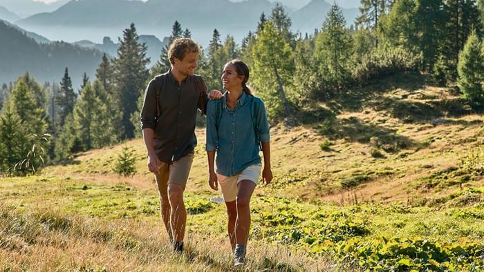 Ein Paar wandert auf einem grasbewachsenen Hügel mit Blick auf Berge und Wälder.
