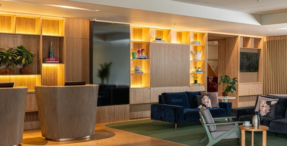 Modern lobby at Habitel Prime Hotel, featuring a plush sofa, a wooden reception desk, and stylish shelving