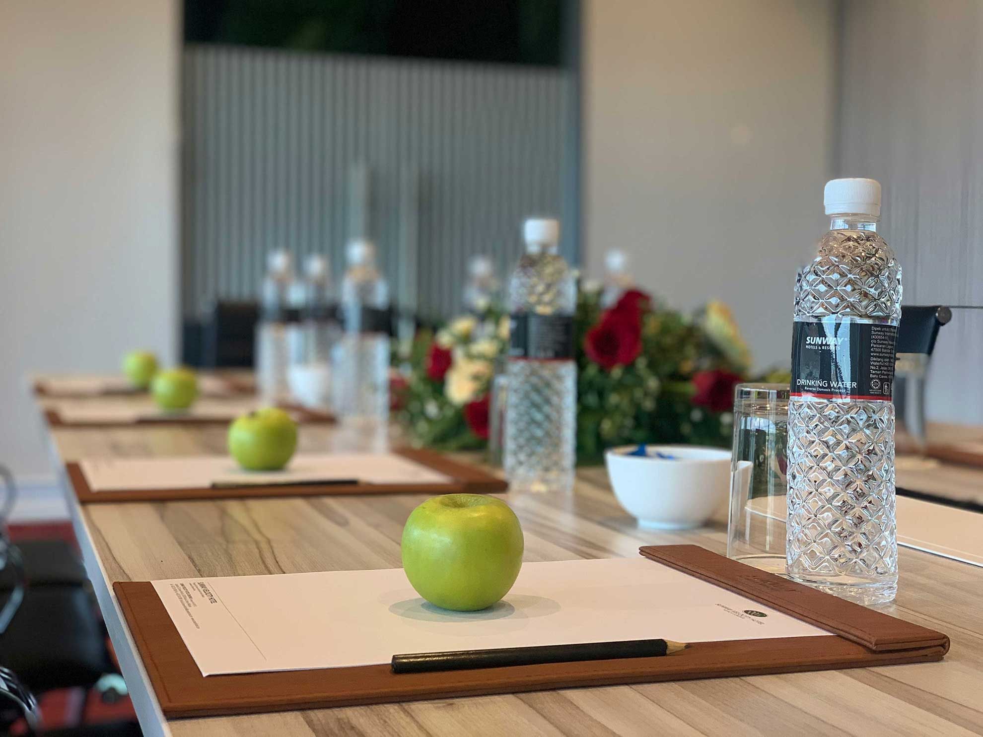 Conference table with water bottles, green apples, notepads, and pens in a meeting room at Sunway Velocity Hotel