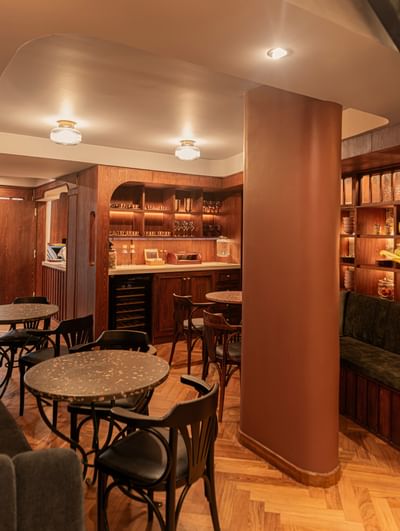 Round tables by black chairs surrounding a large pillar under glowing lamps in 5&Quince Restaurant at 5Q House Chapinero