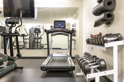 Dumbbells on a white rack by a treadmill at Rodd Miramichi River, an apartment hotel in Miramichi, NB