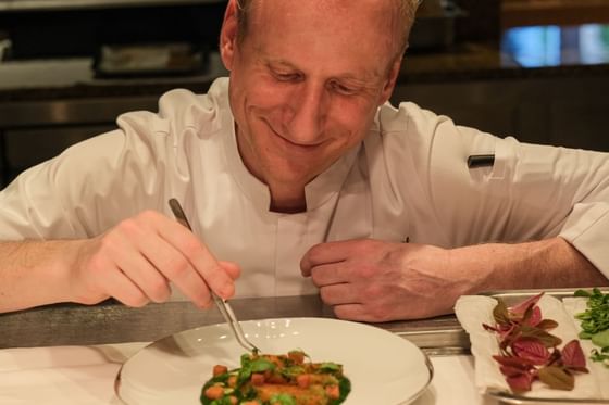 Chef in a white uniform delicately garnishing a dish with vibrant herbs served at Park Hyatt Saigon