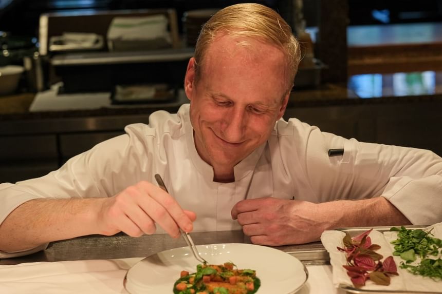Chef in a white uniform delicately garnishing a dish with vibrant herbs served at Park Hyatt Saigon