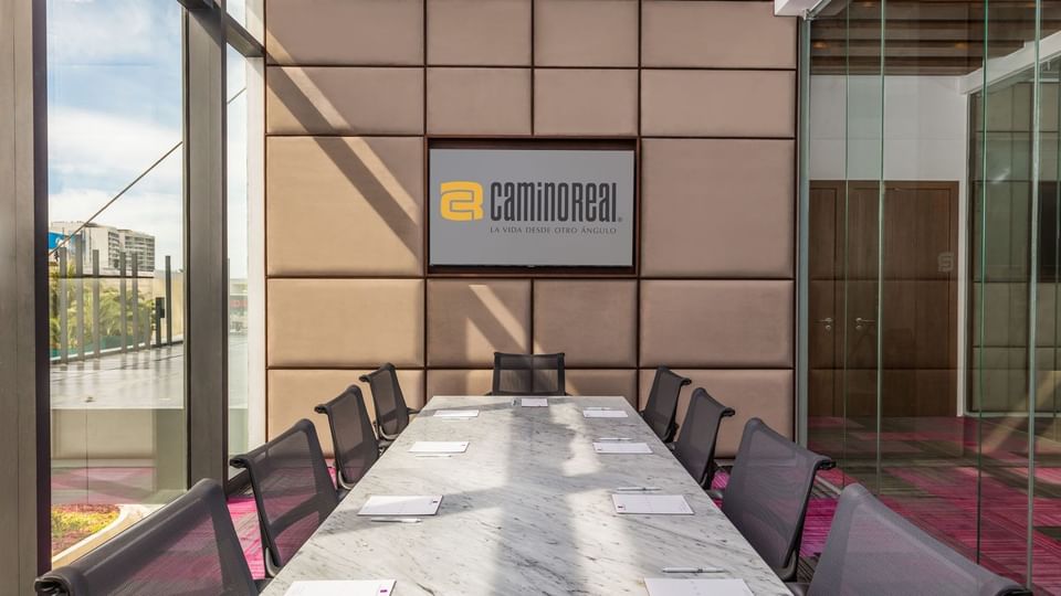 Upscale meeting room featuring a marble table, ergonomic chairs, and a large wall screen at Camino Real Merida