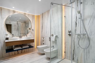 Bathroom featuring a sleek shower, minimalist vanity, round mirror, and warm lighting at Ana Hotels Europa Eforie Nord